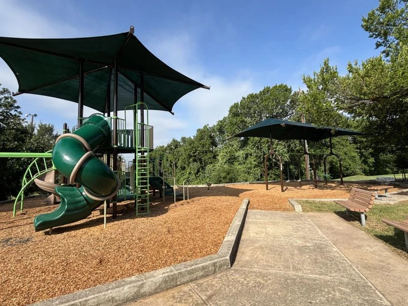 A photo of the new playscape at Metz Neighborhood Park which includes a swing set, a spiral tube slide. climbing features and shade.