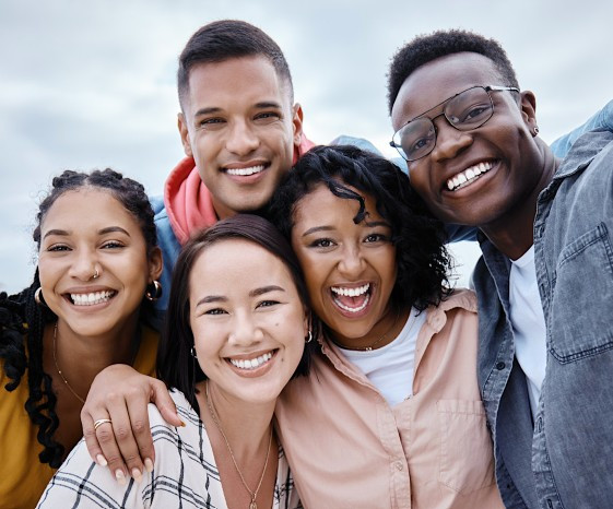 A group of young people of color smile with arms around each other posing for a photo