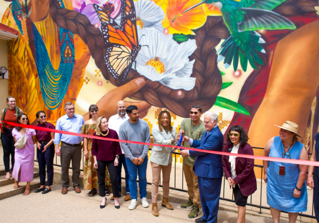 group of people cutting a ribbon in front of a mural