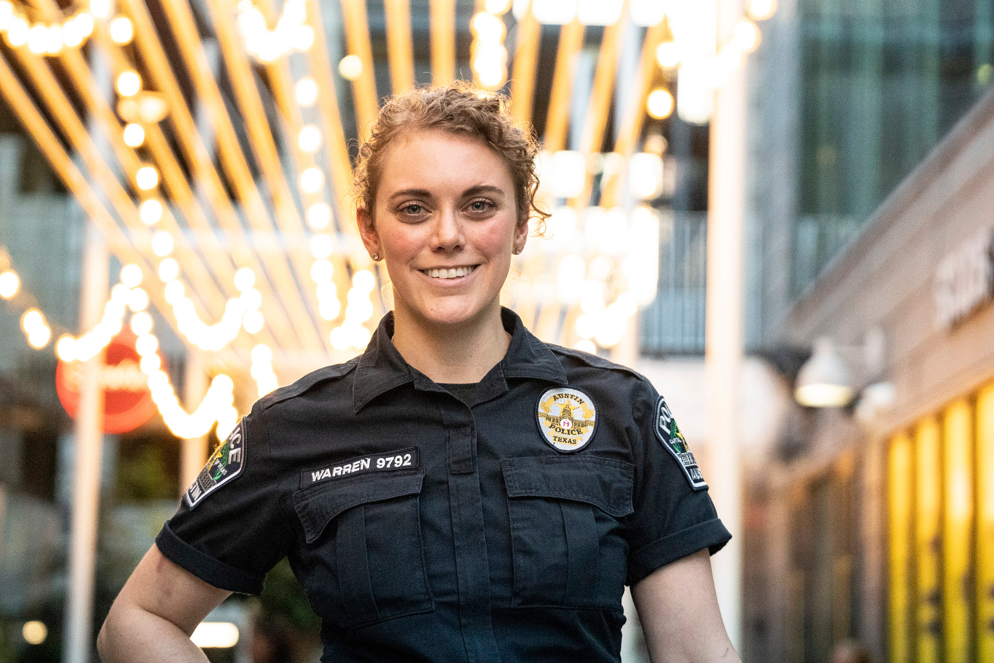 A female Austin Police Officer stands in front of a well-let business.