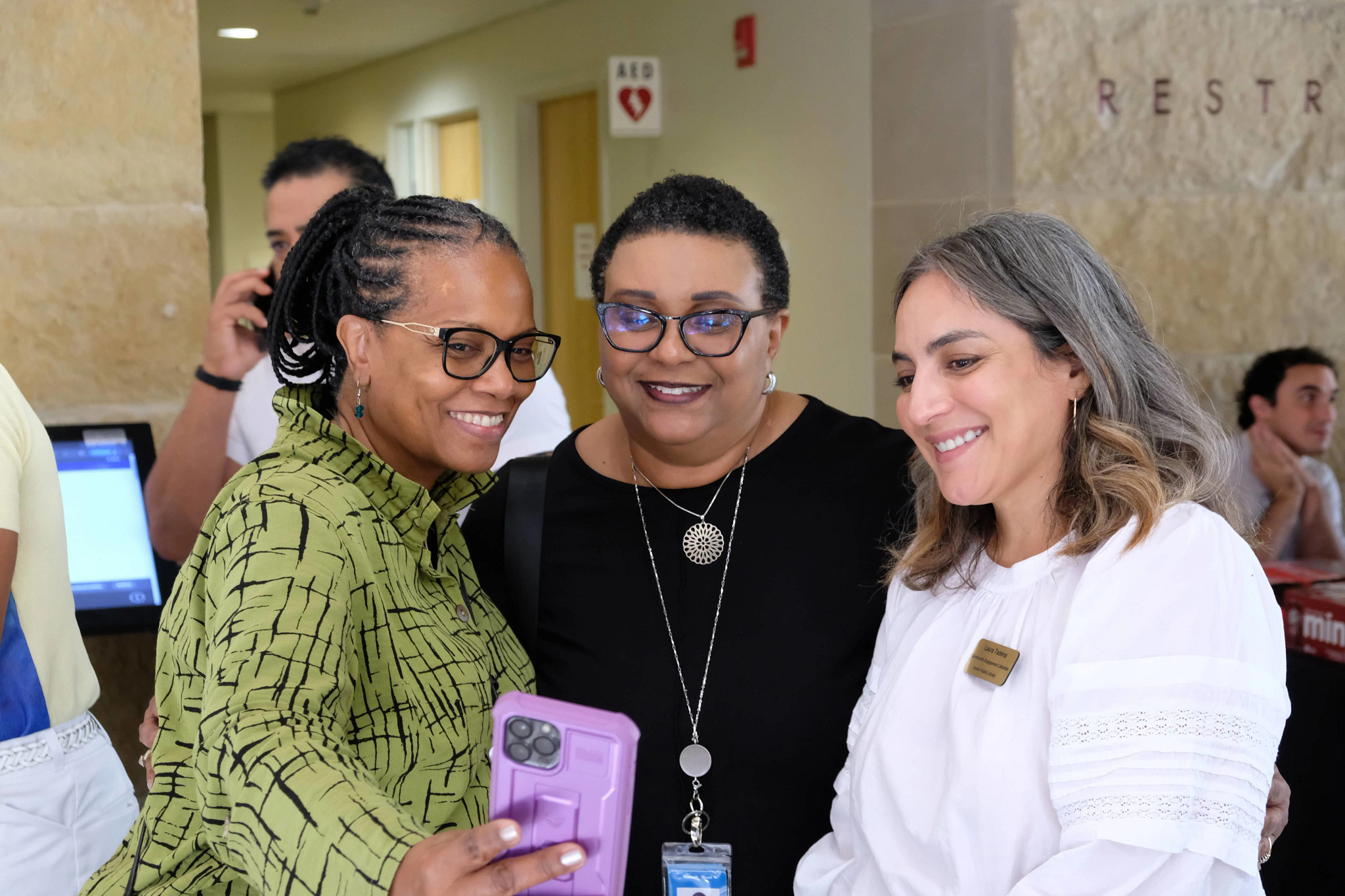 Two Black women and at Latino woman smile big for a selfie at City Hall after Welcoming Week cermony and proclamation