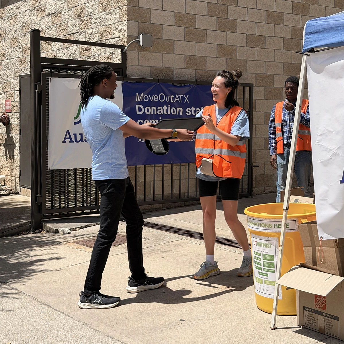 A person hands off a donation to a MoveOutATX volunteer at a donation station.