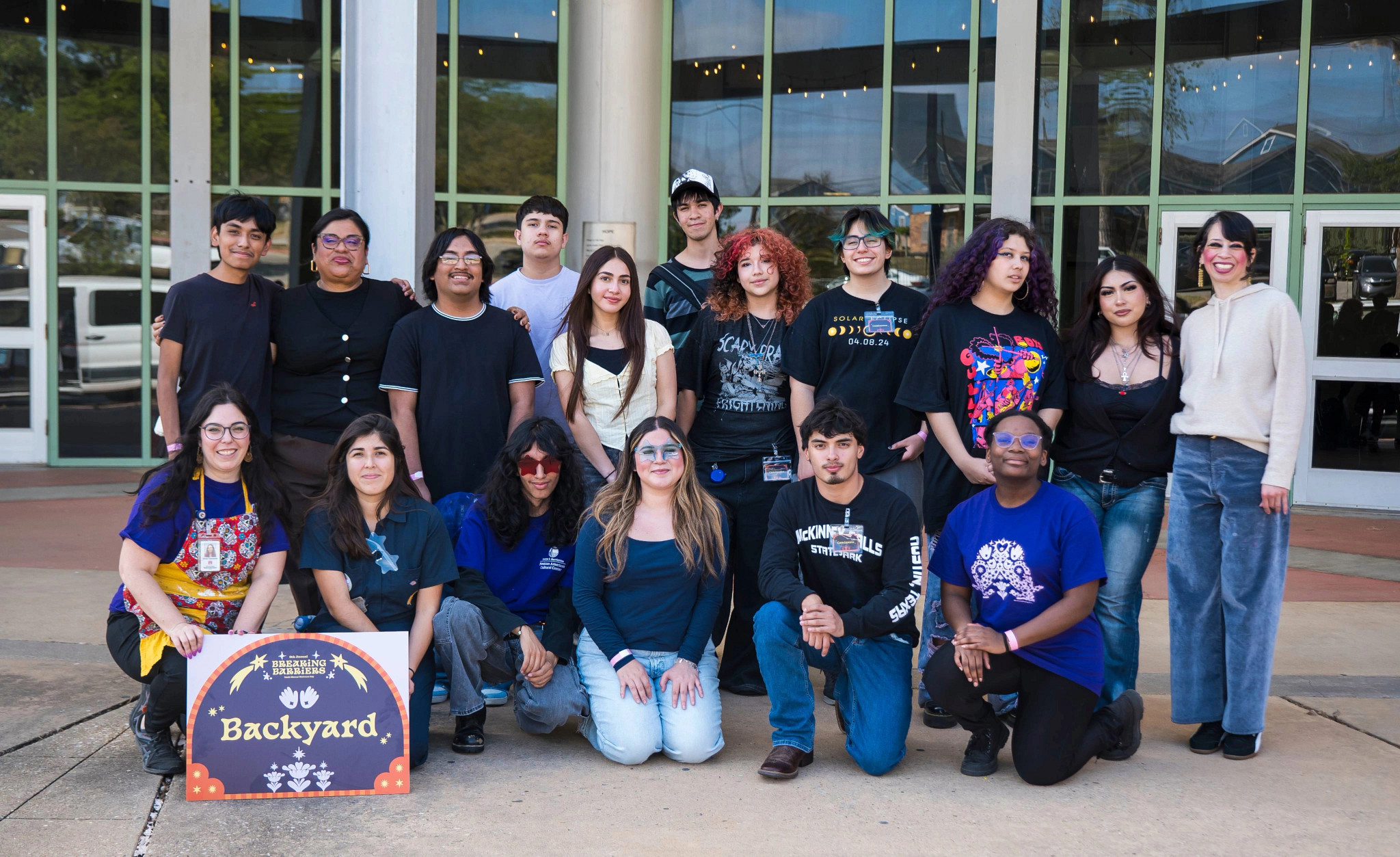 Group of teens and adults smile for a picture in front of a building