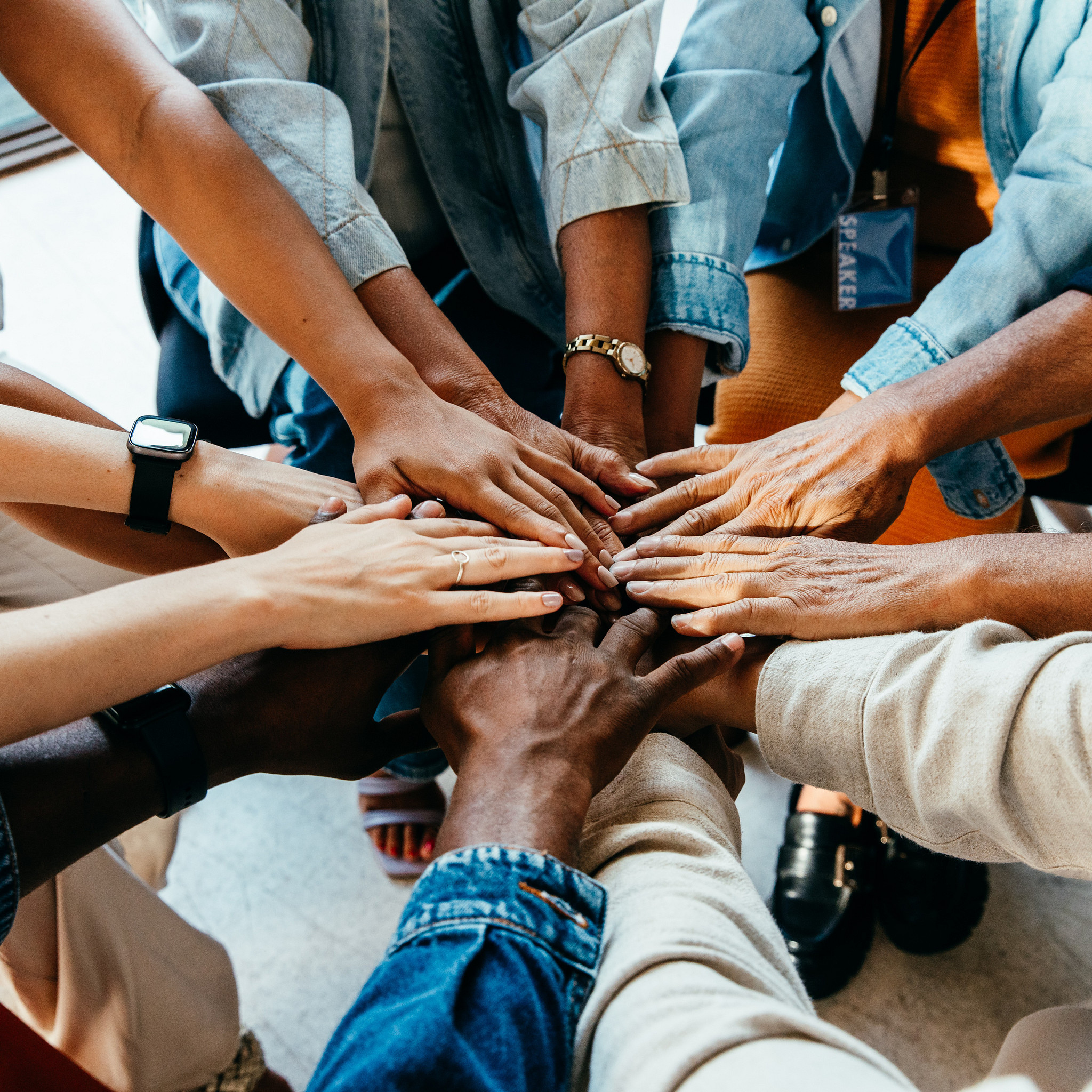 A diverse group of people in a circle with their hands in the middle.