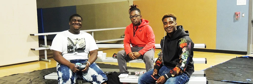 Three teenage boys sitting on bleachers playing on hand held equipment.