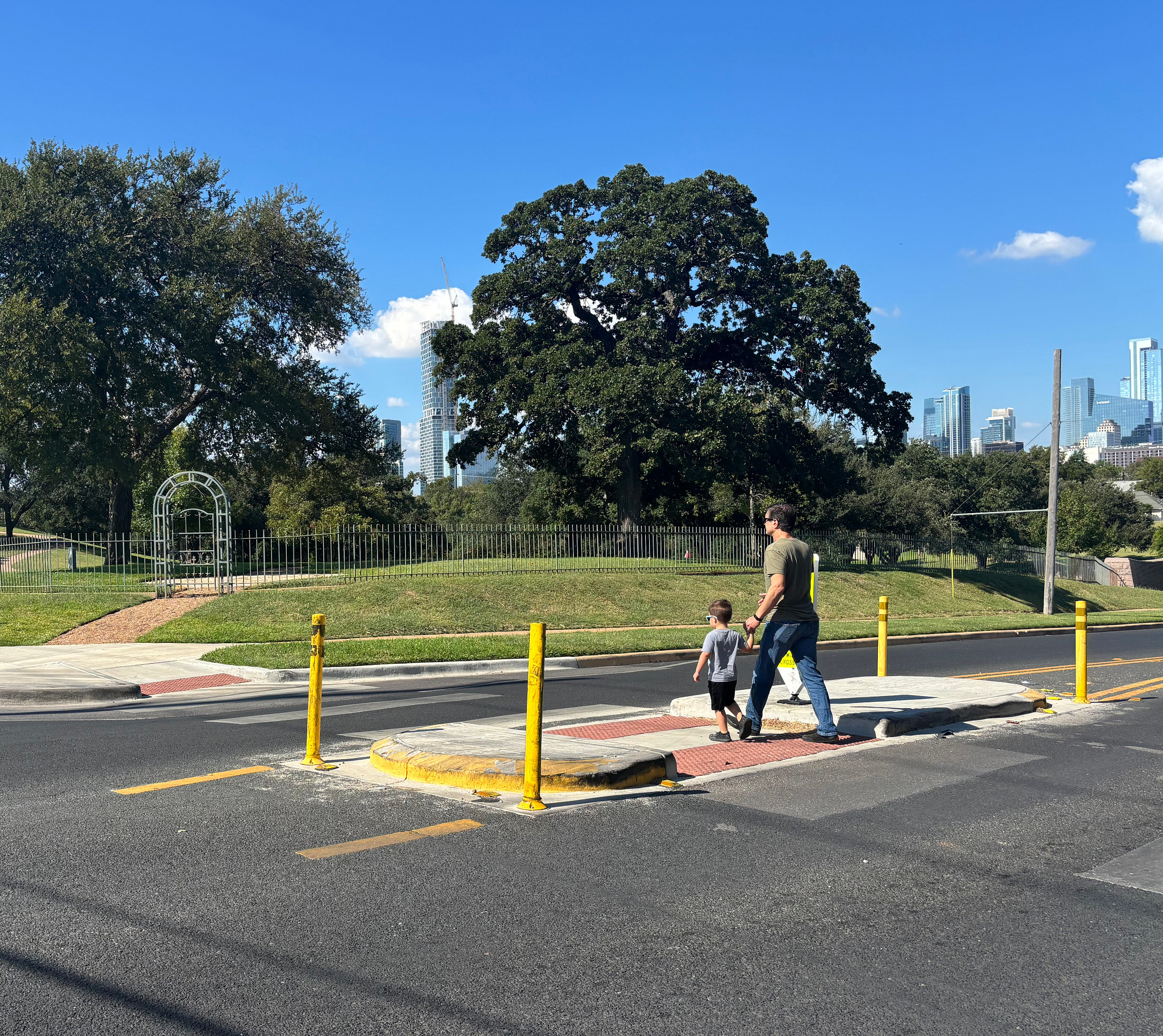 Adult and child walk across a street with a pedestrian crossing island.