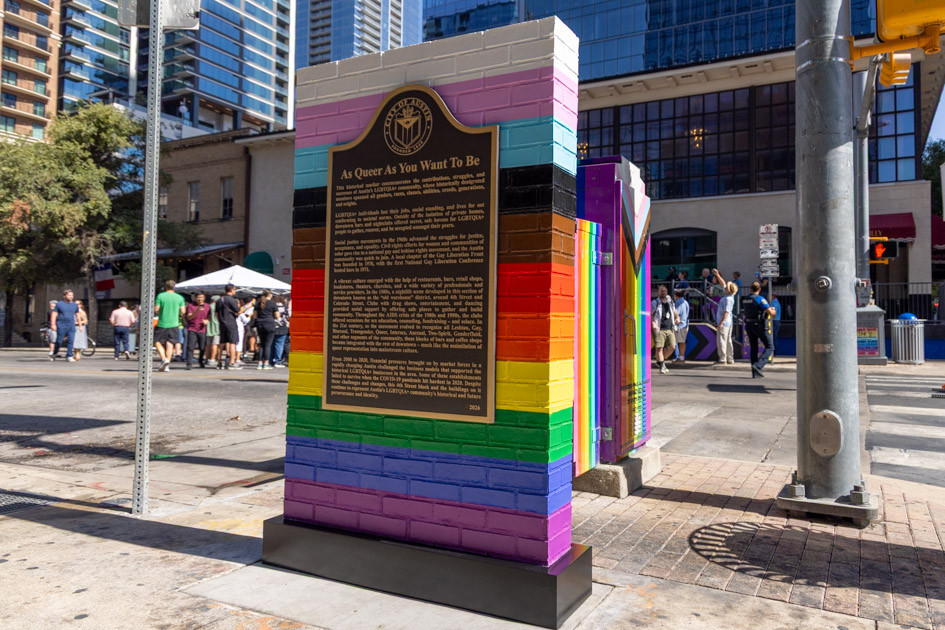 A brick marker on the sidewalk painted in rainbow colors