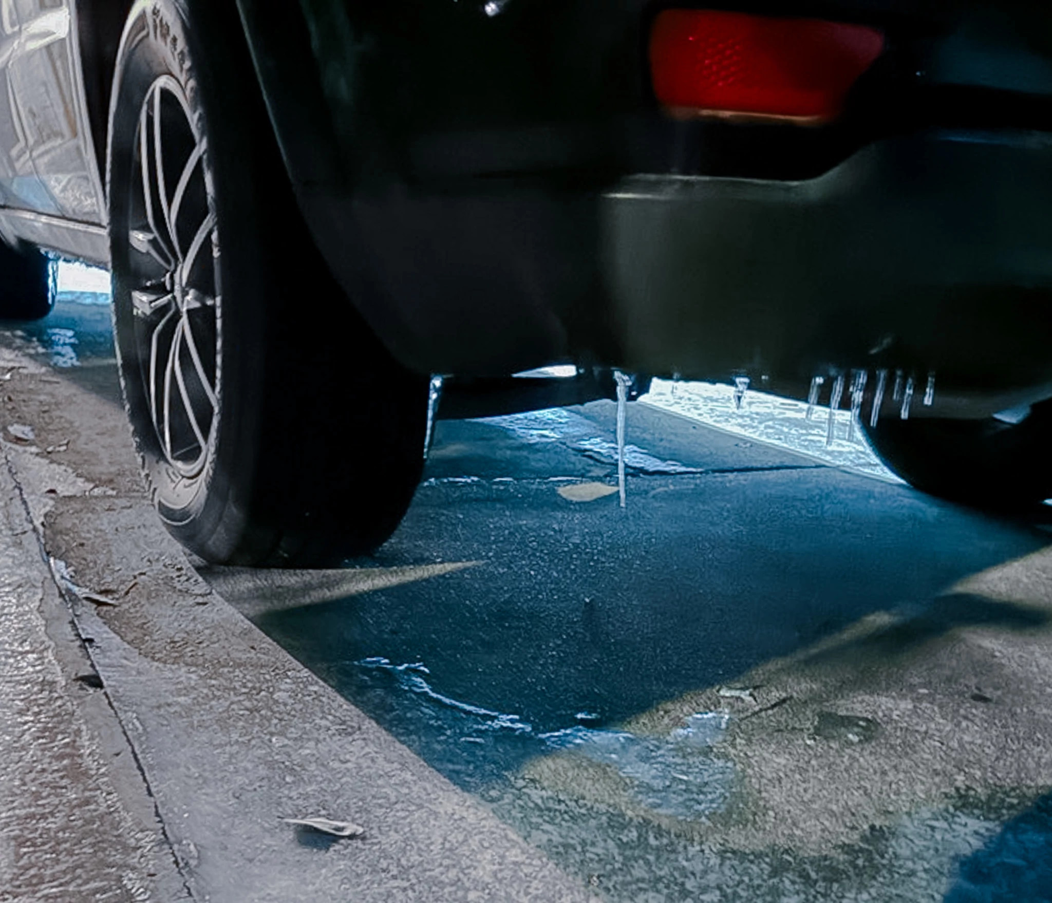 View of frozen bumper and tires of an SUV with icicles and frozen ground around it