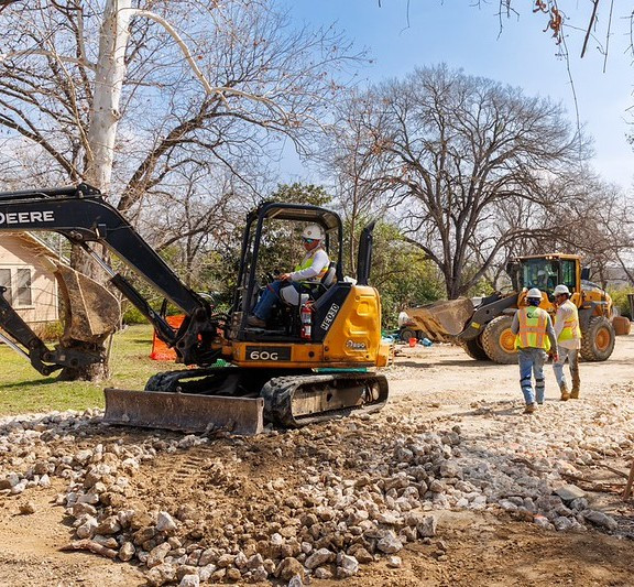 Heavy equipment and construction workers on unpaved, residential street