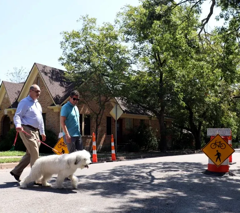 Two people walk with a dog on a Living Street in Austin.