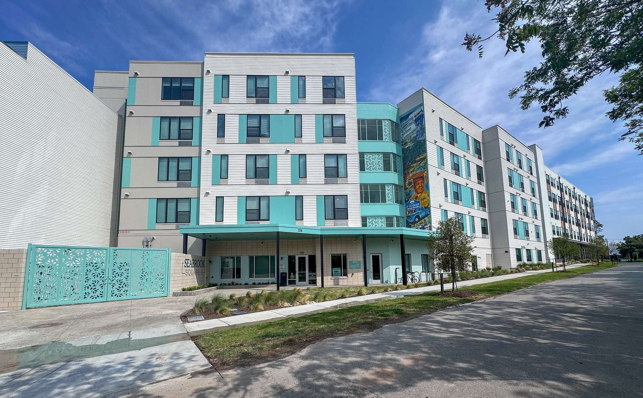 Exterior view of Seabrook Square II, a PSH community in East Austin, with a decorative gate, mural, and landscaped walkway. 