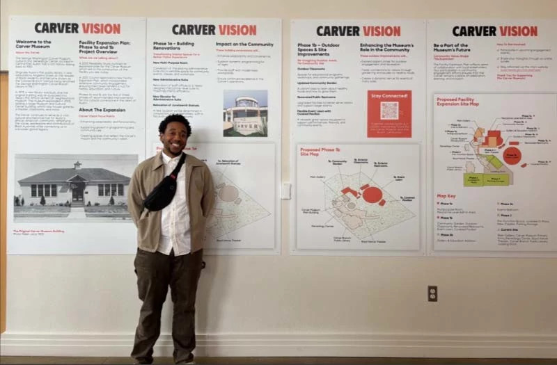 Image of Carver Vision boards in background at Carver Museum with community member smiling