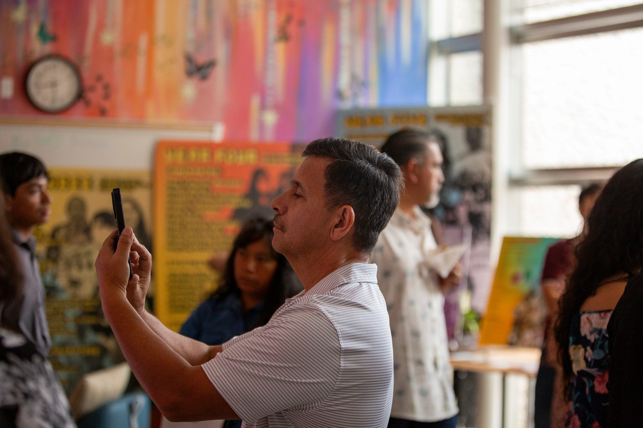 Man holding up his phone in a room with colorful artworks 