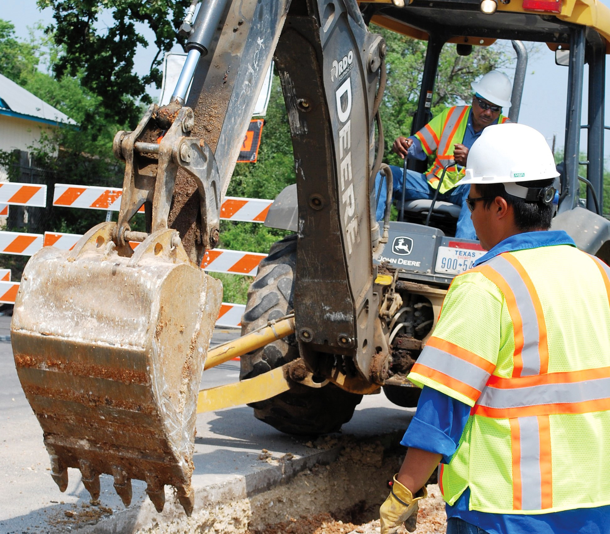 Two Austin Water workers using an excavator to dig for pipelines under a street.