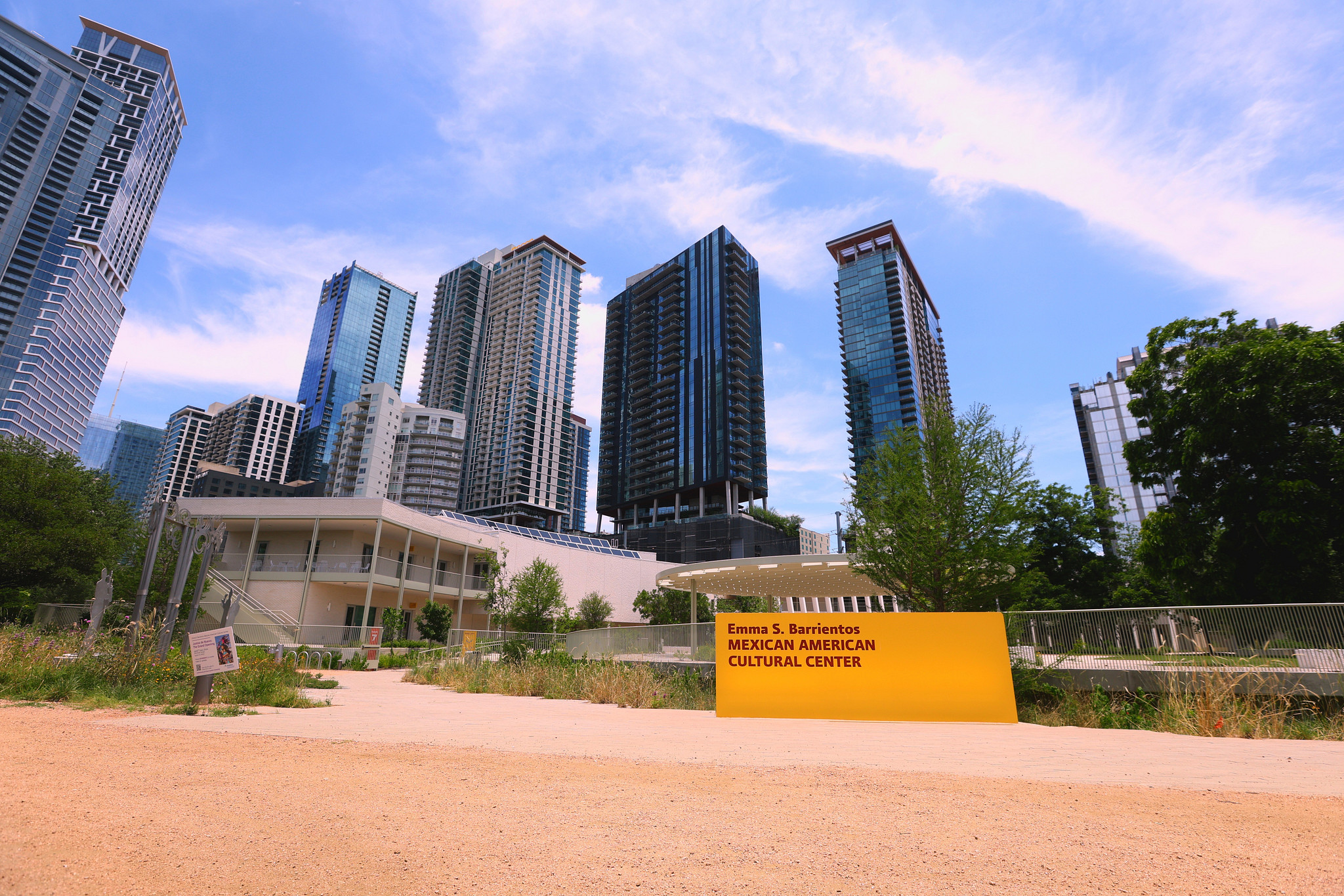 Photo of the yellow MACC sign at the Trail with skyscrapers and blue sky