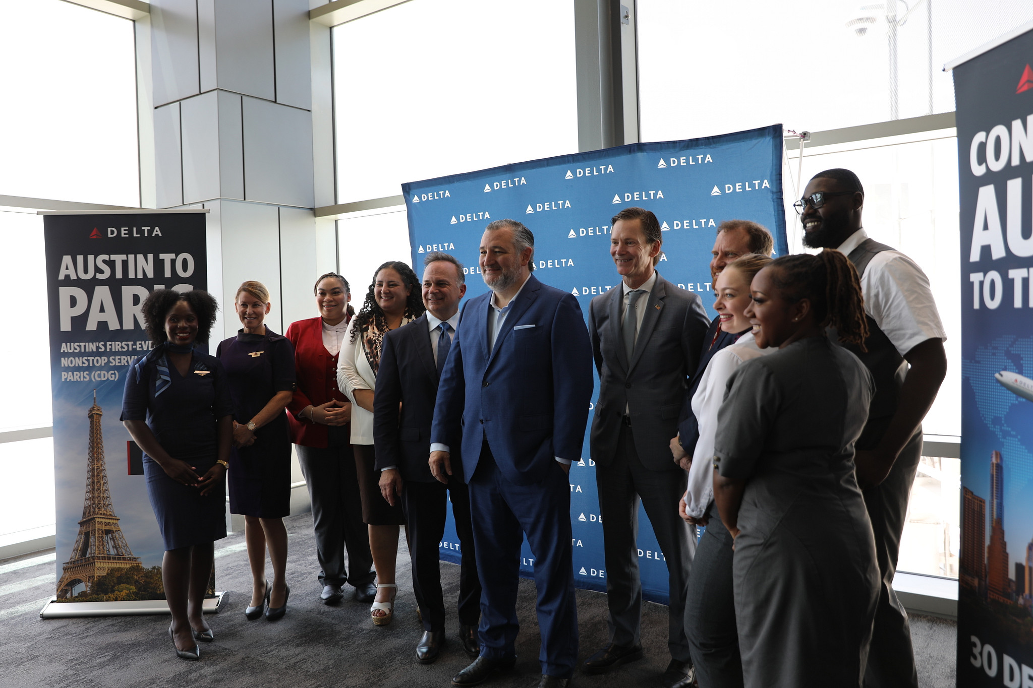 A group of people stand together indoors in front of Delta branded banners for a photo. Signs on each side promote nonstop flights from Austin to Paris.