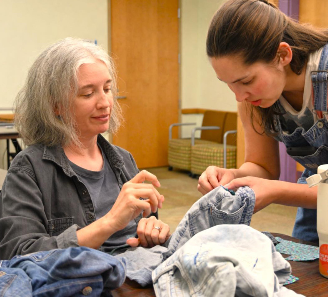Two women mend denim items.