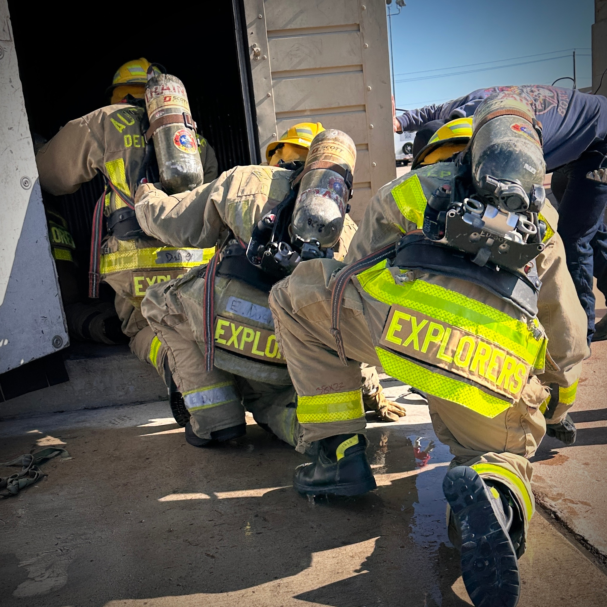 Four Austin Fire Explorers in full firefighting gear navigating entryway into building during simulated black-out conditios