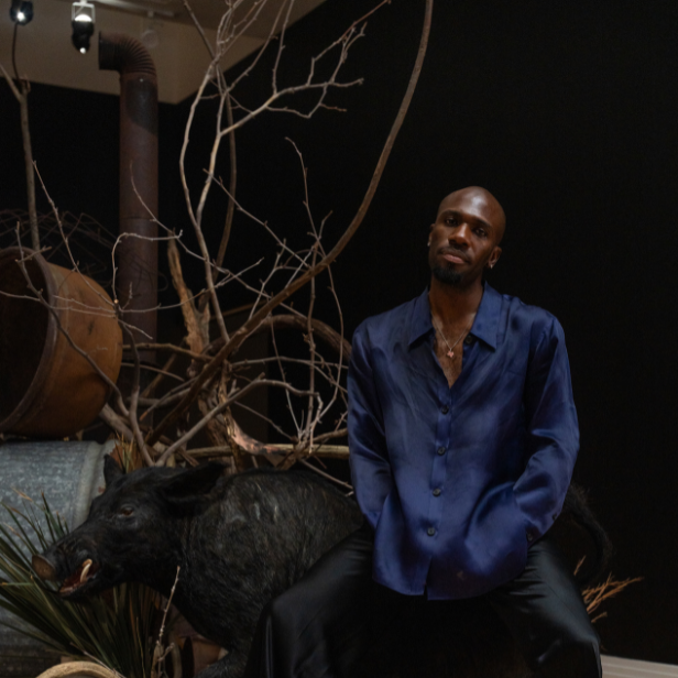 Image of artist Hakeem Adewumi seated in front of his artwork at the George Washington Carver Museum