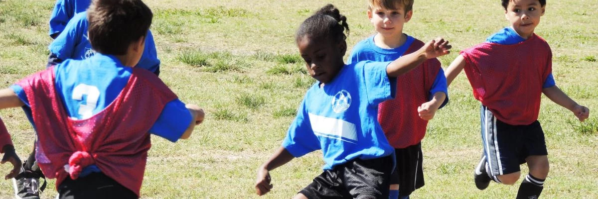 Girl kicking the soccer ball while opposing players come toward her.