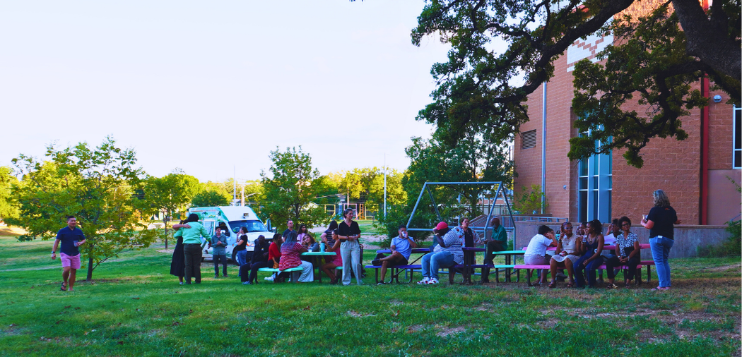 People gather together around picnic tables under a large oak tree for the Resilience Mini Grant Ice Cream Social.