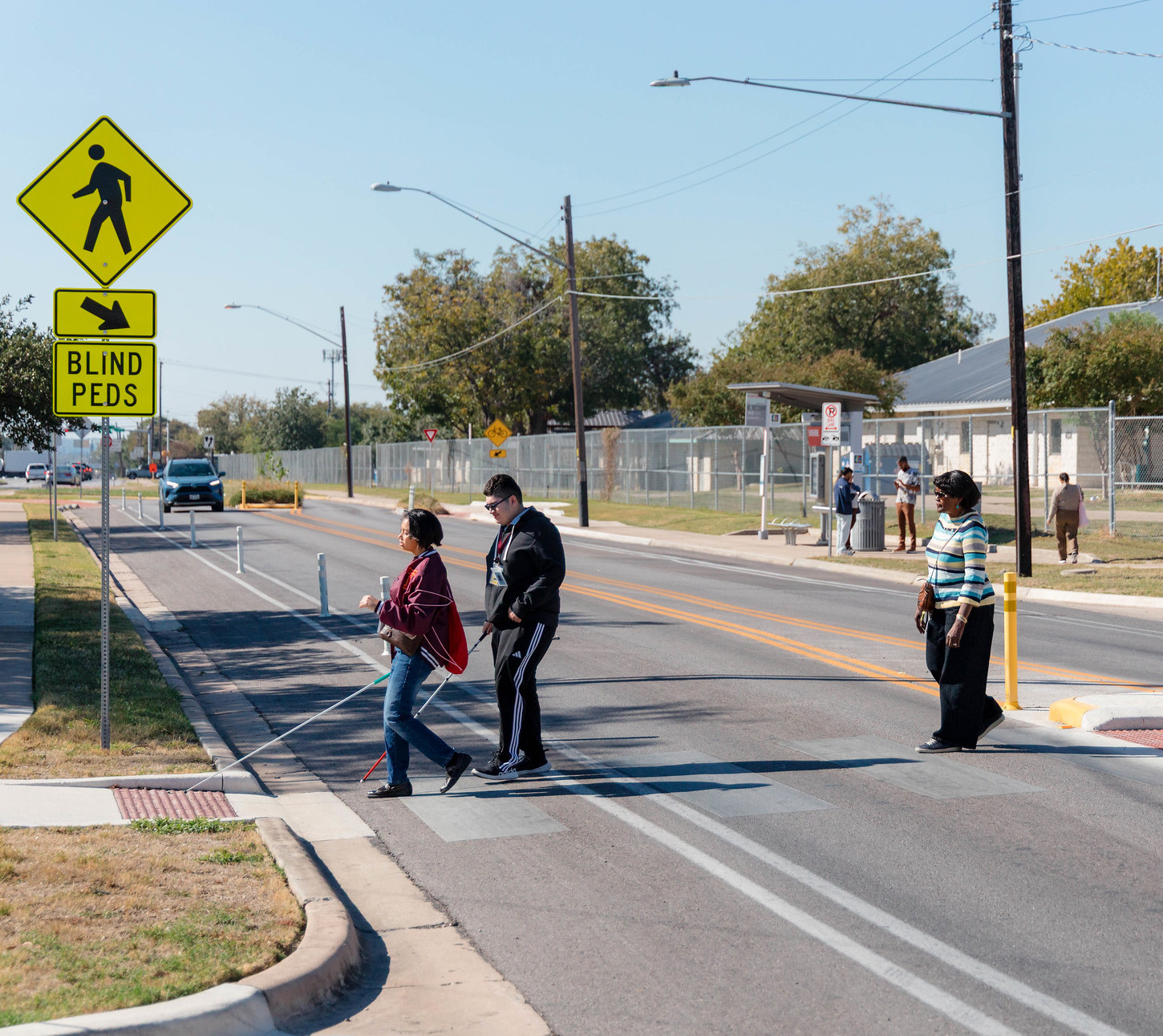 People cross Sunshine Drive at a crosswalk with a crossing island.