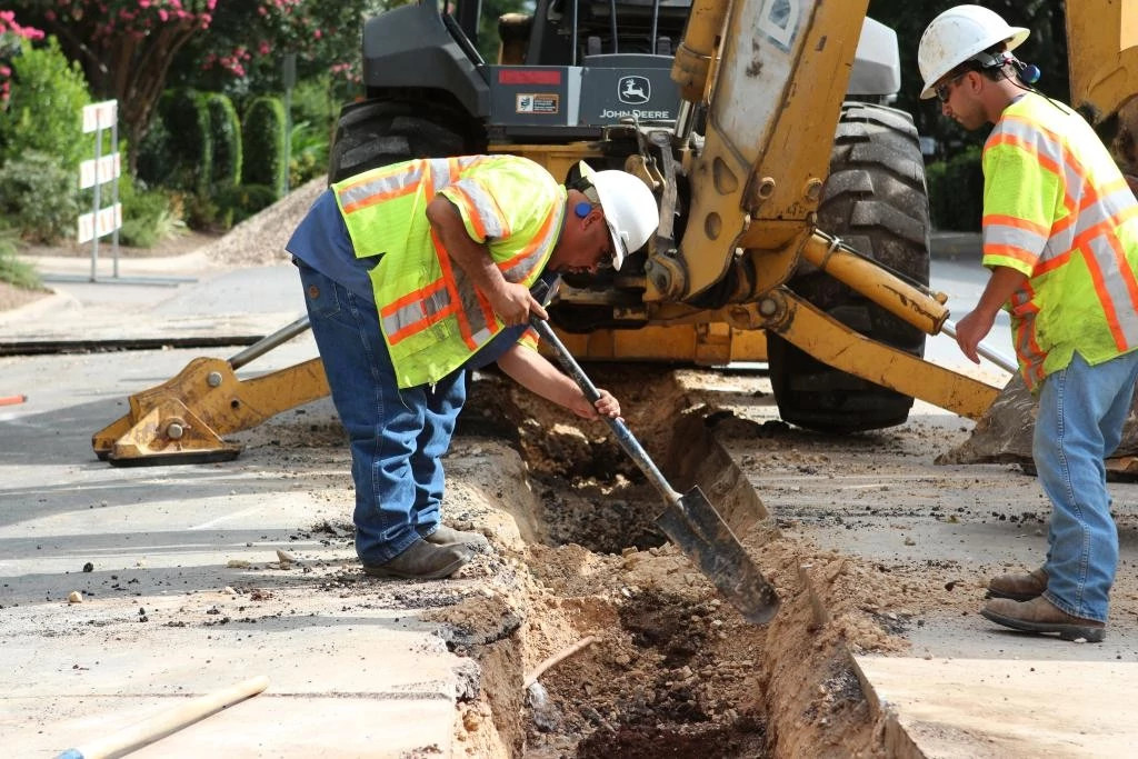 A view of two Austin Water workers using construction machinery to excavate an underground water pipe beneath the street.