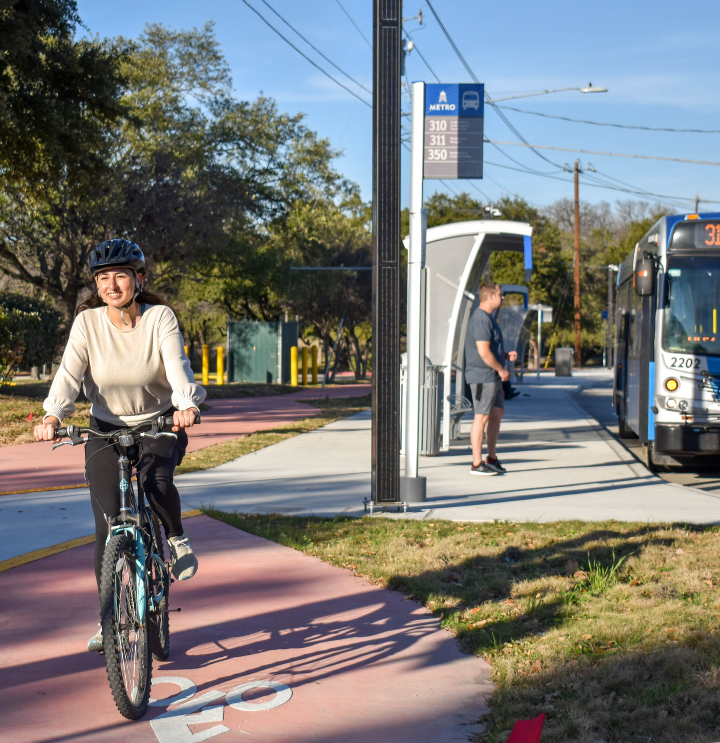 A women in the foreground using a bike lane. A person waits to board a CapMetro bus in the background.